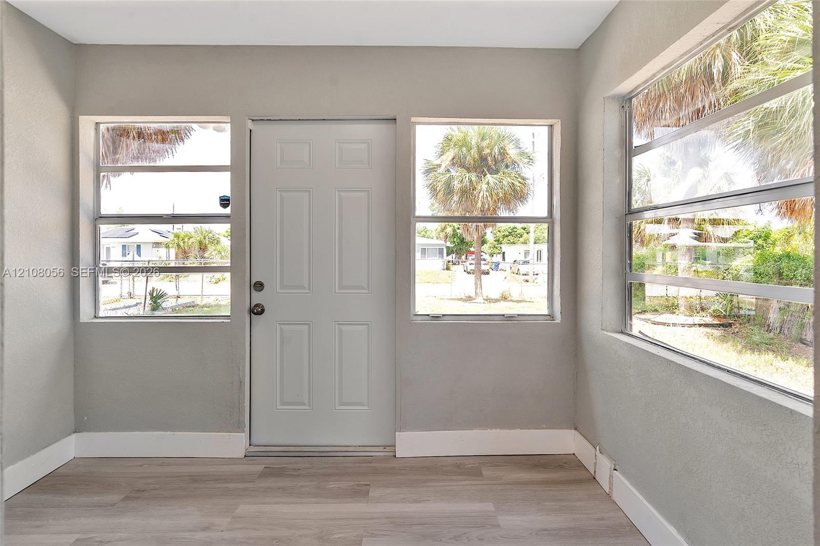 Neutral-toned interior featuring wood-finish flooring, three large windows with horizontal panes, and a six-panel entry door
