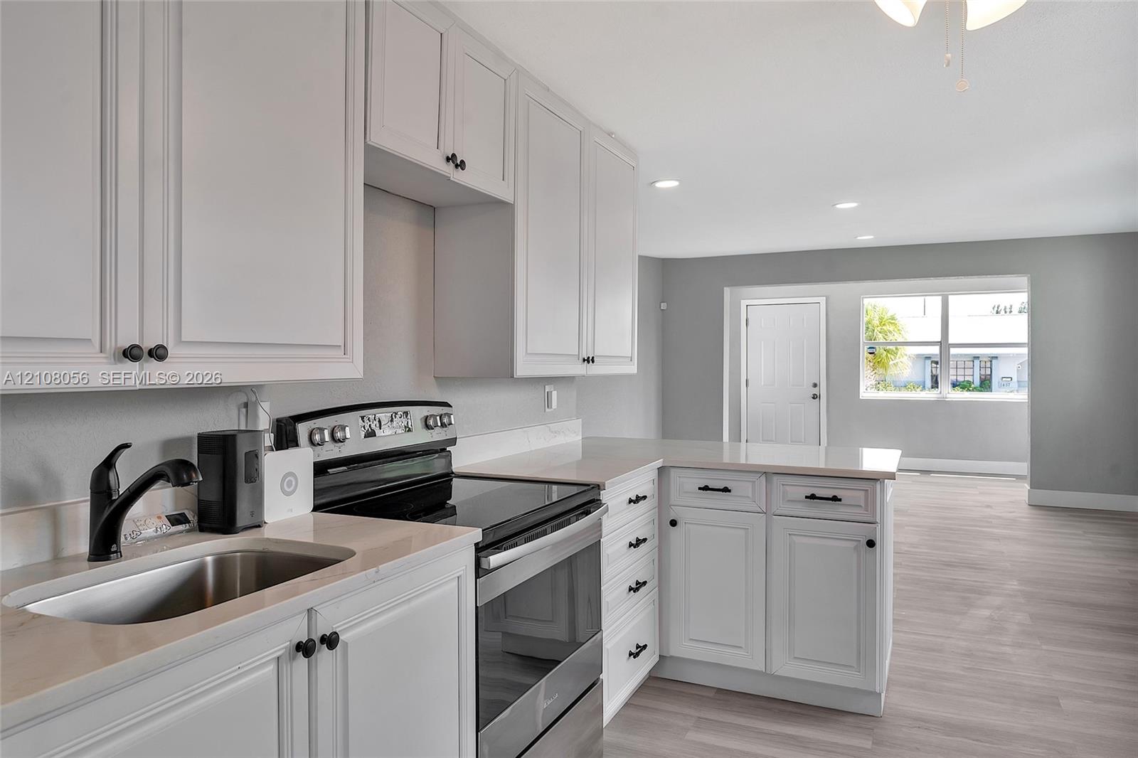 Kitchen featuring shaker-style cabinetry, solid surface countertops, stainless steel electric range, undermount sink with matte black faucet, and wood-finish flooring