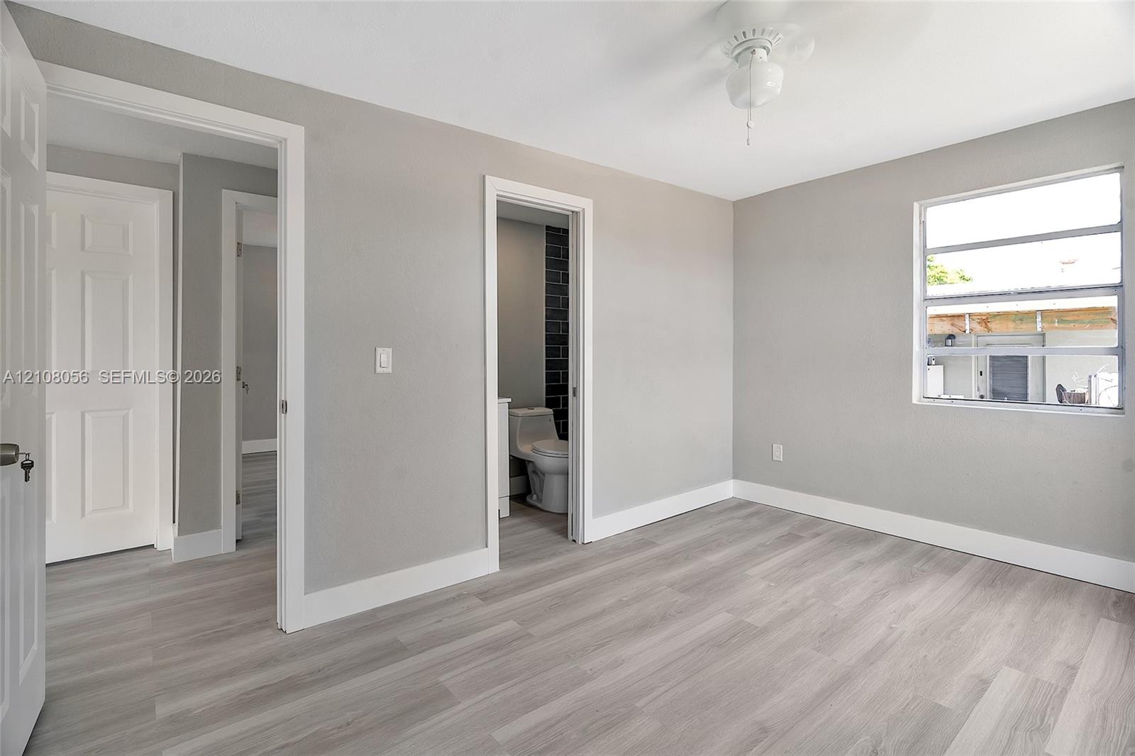 Neutral-toned interior room featuring wood-finish flooring, a ceiling fan, and white-paneled interior doors