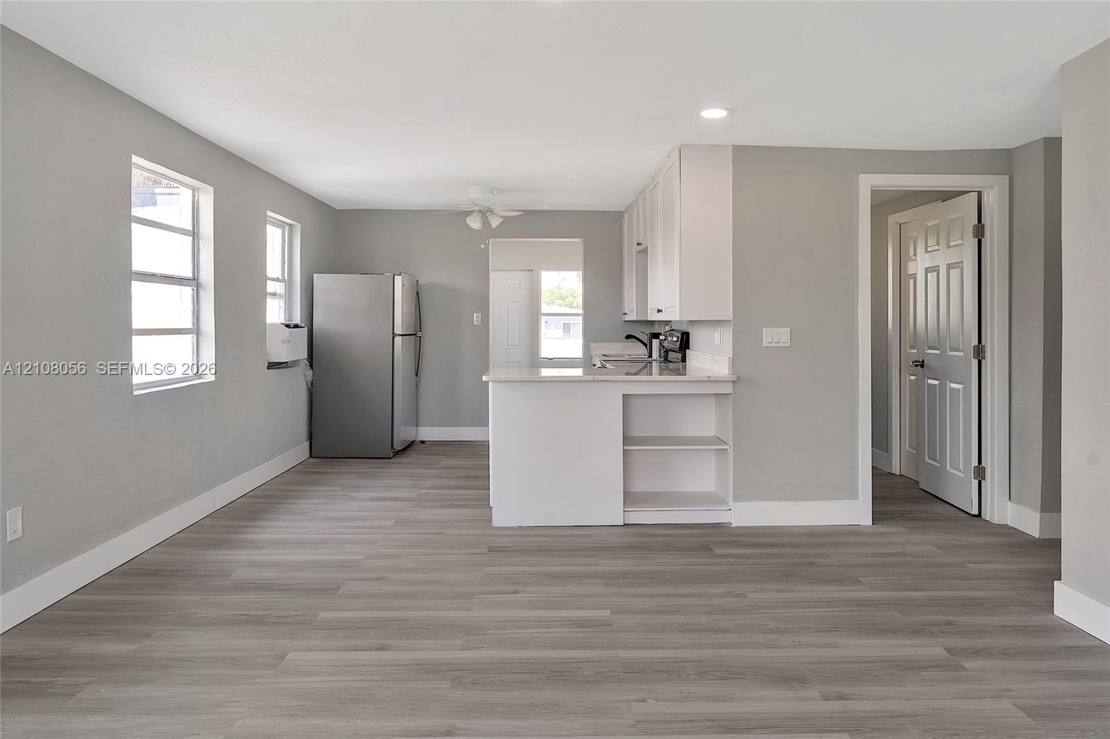 Kitchen area featuring white cabinetry, a peninsula with built-in shelving, wood-finish flooring, recessed lighting, and stainless steel refrigerator