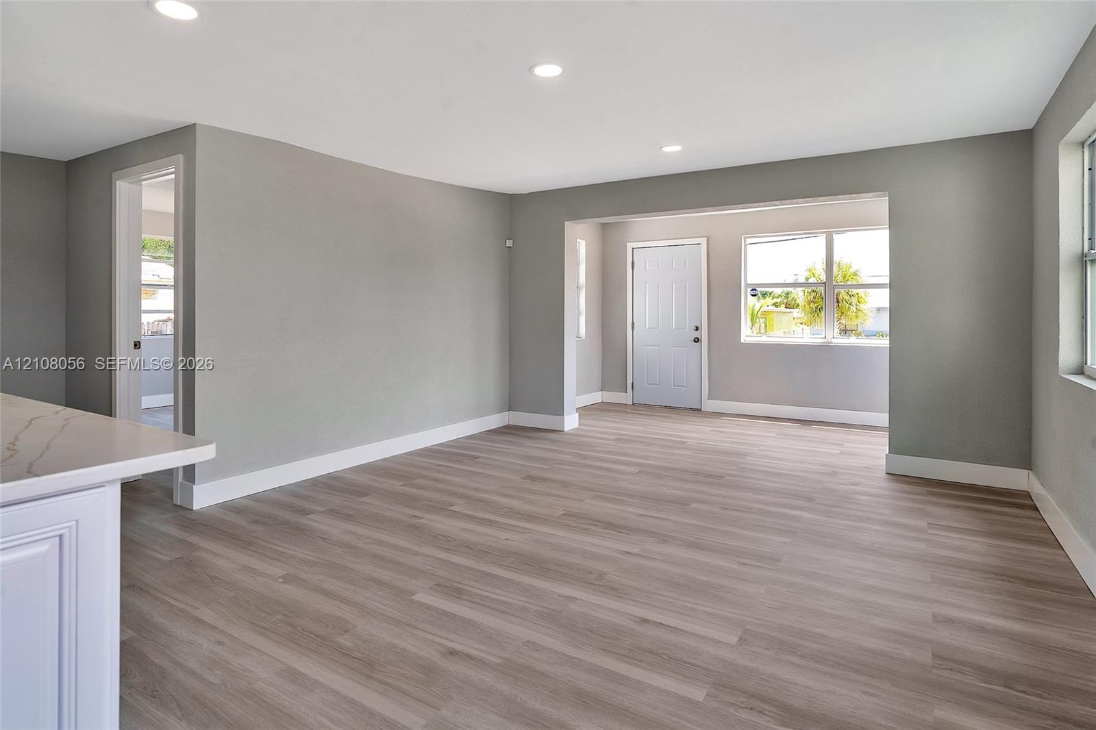 Open-concept living space featuring wood-finish flooring, recessed lighting, white cabinetry with a light-toned stone-finish countertop, and windows with natural light