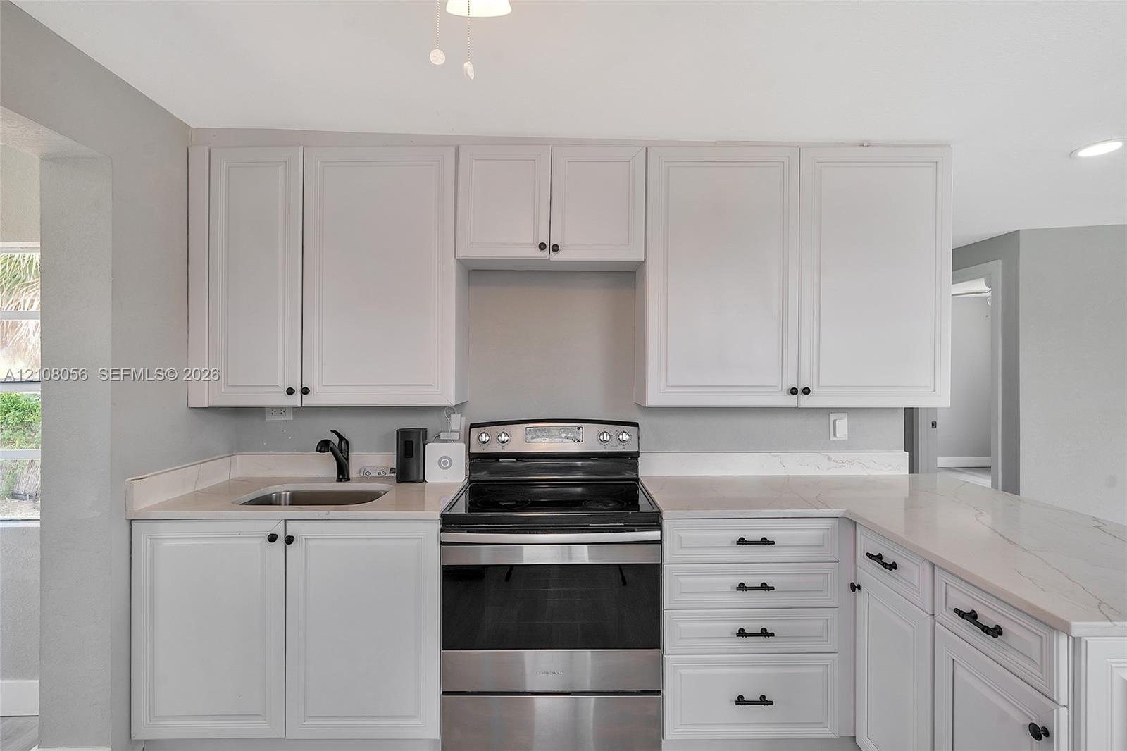 Kitchen featuring white shaker-style cabinetry, light-toned stone countertops, stainless steel electric range, undermount sink with a matte black faucet, and coordinating matte black hardware