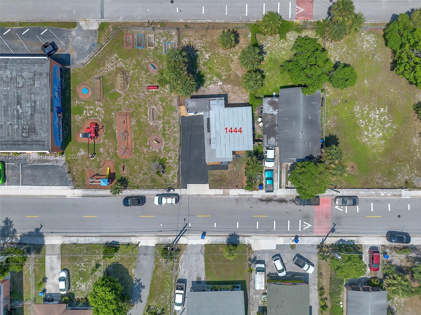Aerial perspective of a property featuring an asphalt driveway, paved exterior areas, and surrounding mature trees