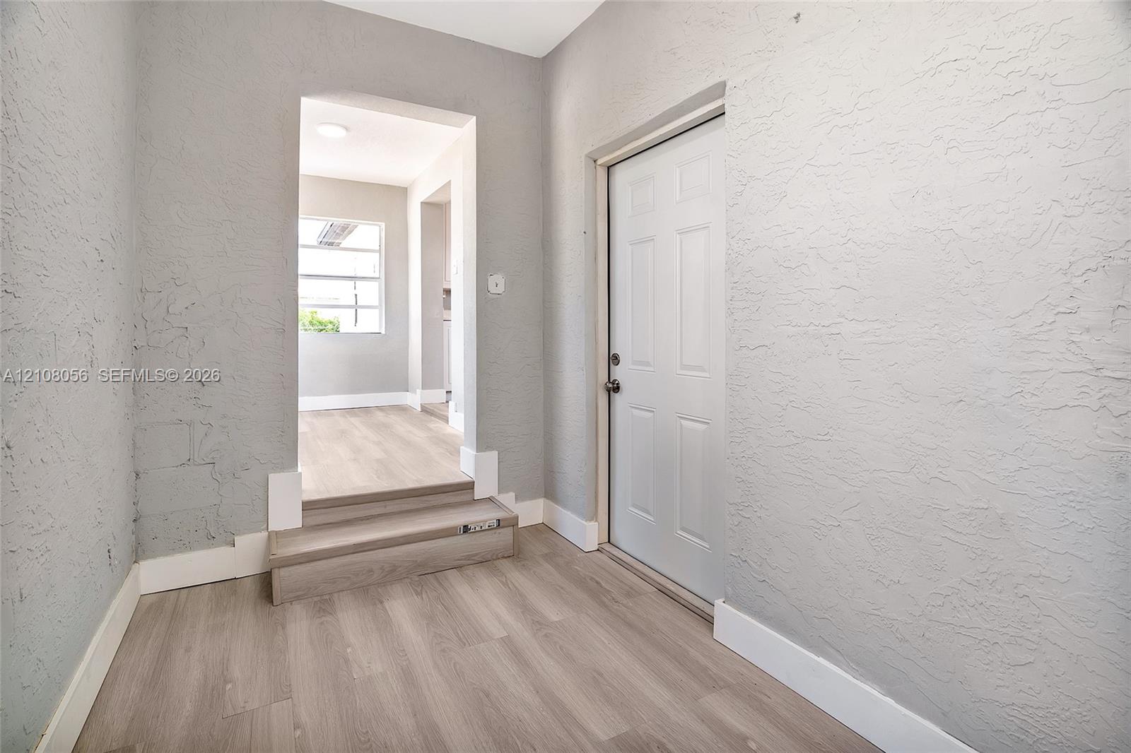 Interior space featuring wood-finish flooring, a multi-panel door, and textured walls