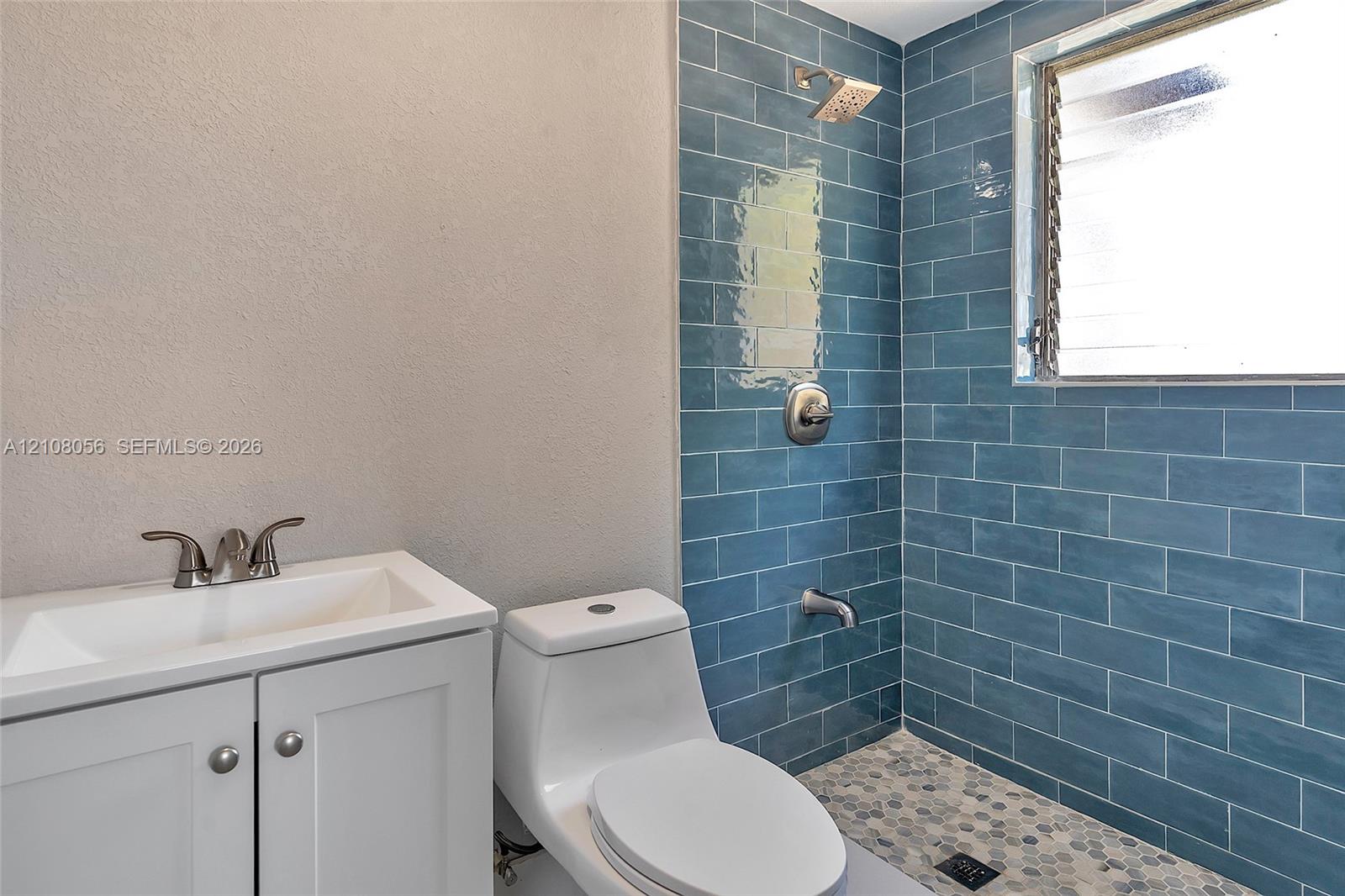 Bathroom featuring blue subway wall tile, pebble-stone flooring, white cabinetry, integrated sink, and polished chrome fixtures