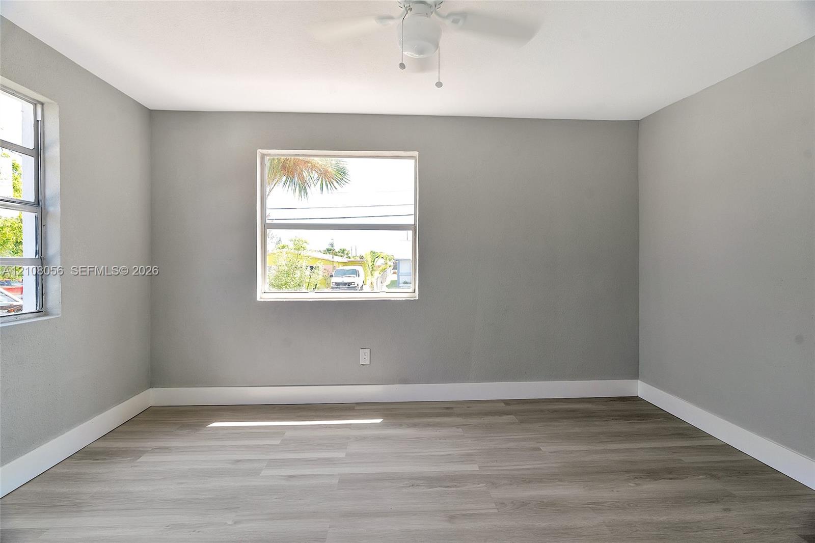 Room featuring neutral-toned walls, wood-finish flooring, and a ceiling-mounted fan with integrated lighting