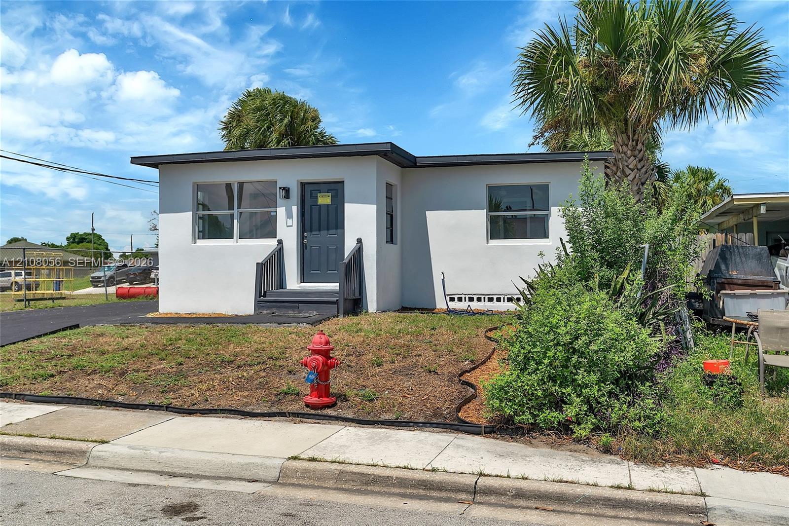 Single-story exterior featuring a white stucco facade, flat roofline, dark-toned entry door, and paved driveway