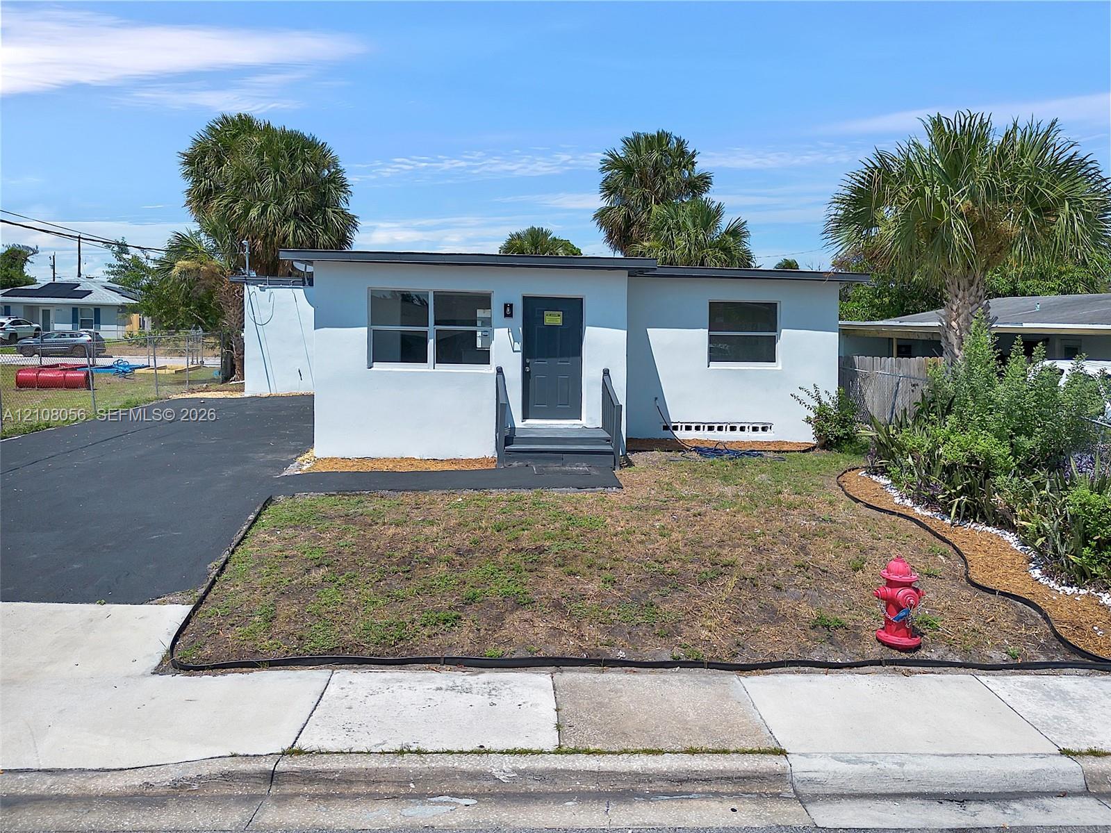 Single-story exterior featuring a light-toned smooth finish, dark-toned entry door, asphalt driveway, and metal-framed windows