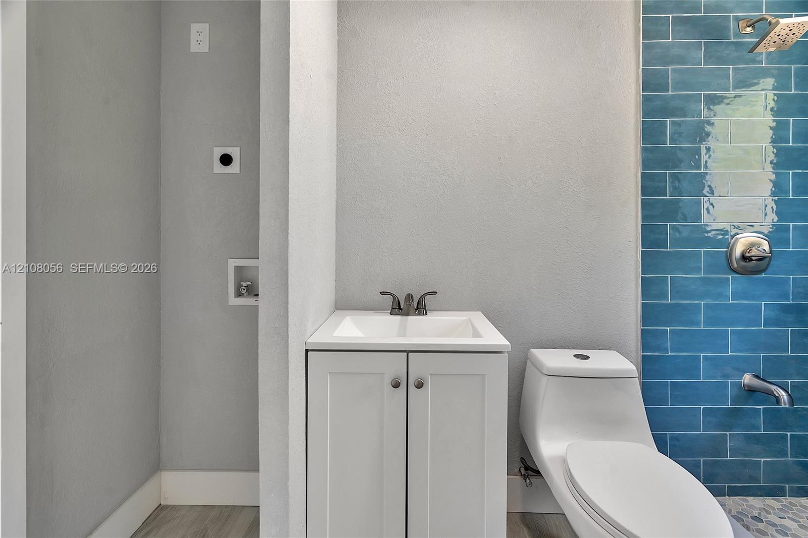 Bathroom featuring a white vanity cabinet with a rectangular basin, metallic dual-handle faucet, one-piece toilet, and blue subway tile shower surround with chrome fixtures