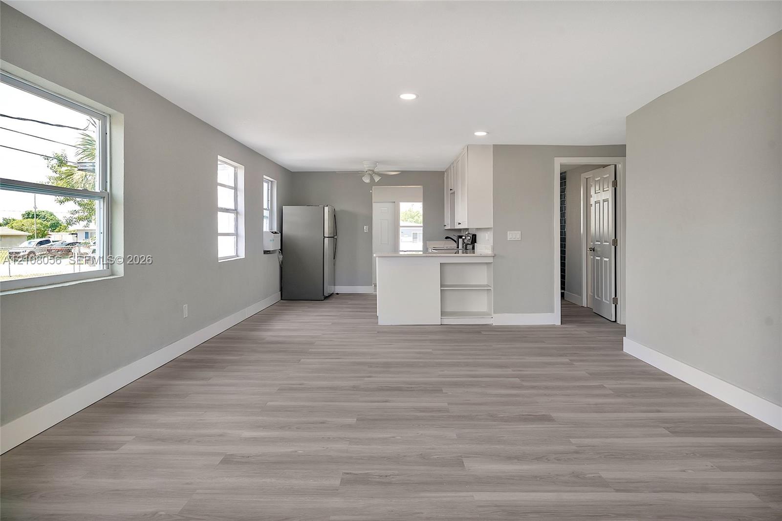 Open-concept interior featuring wood-finish flooring, recessed lighting, and white cabinetry with a built-in peninsula
