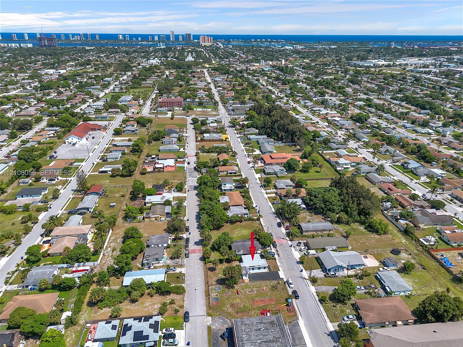 Aerial perspective of a corner lot property featuring an asphalt-shingled roof and exterior hardscaping, situated in proximity to coastal waterfront and urban infrastructure