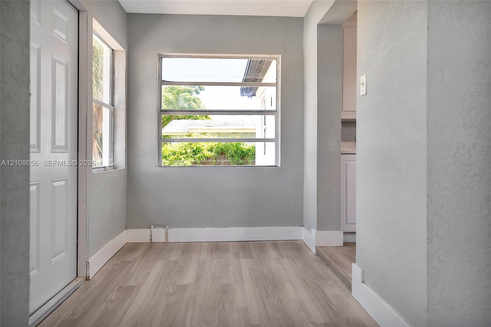 Neutral-toned interior space featuring wood-finish flooring, multi-pane windows, and a solid-panel door