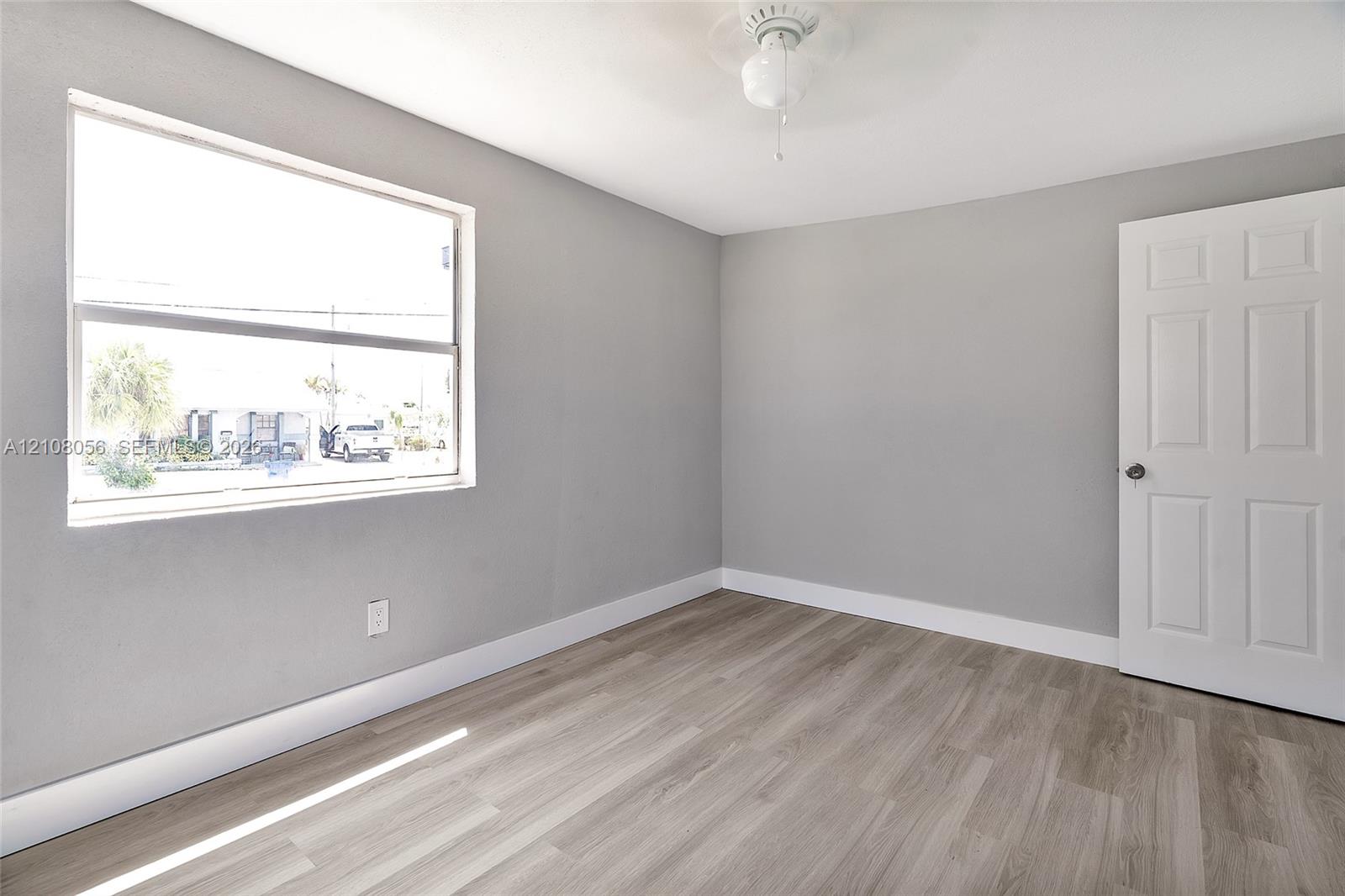 Neutral-toned interior featuring wood-finish flooring, a large single-pane window, and a six-panel door with brushed metal hardware