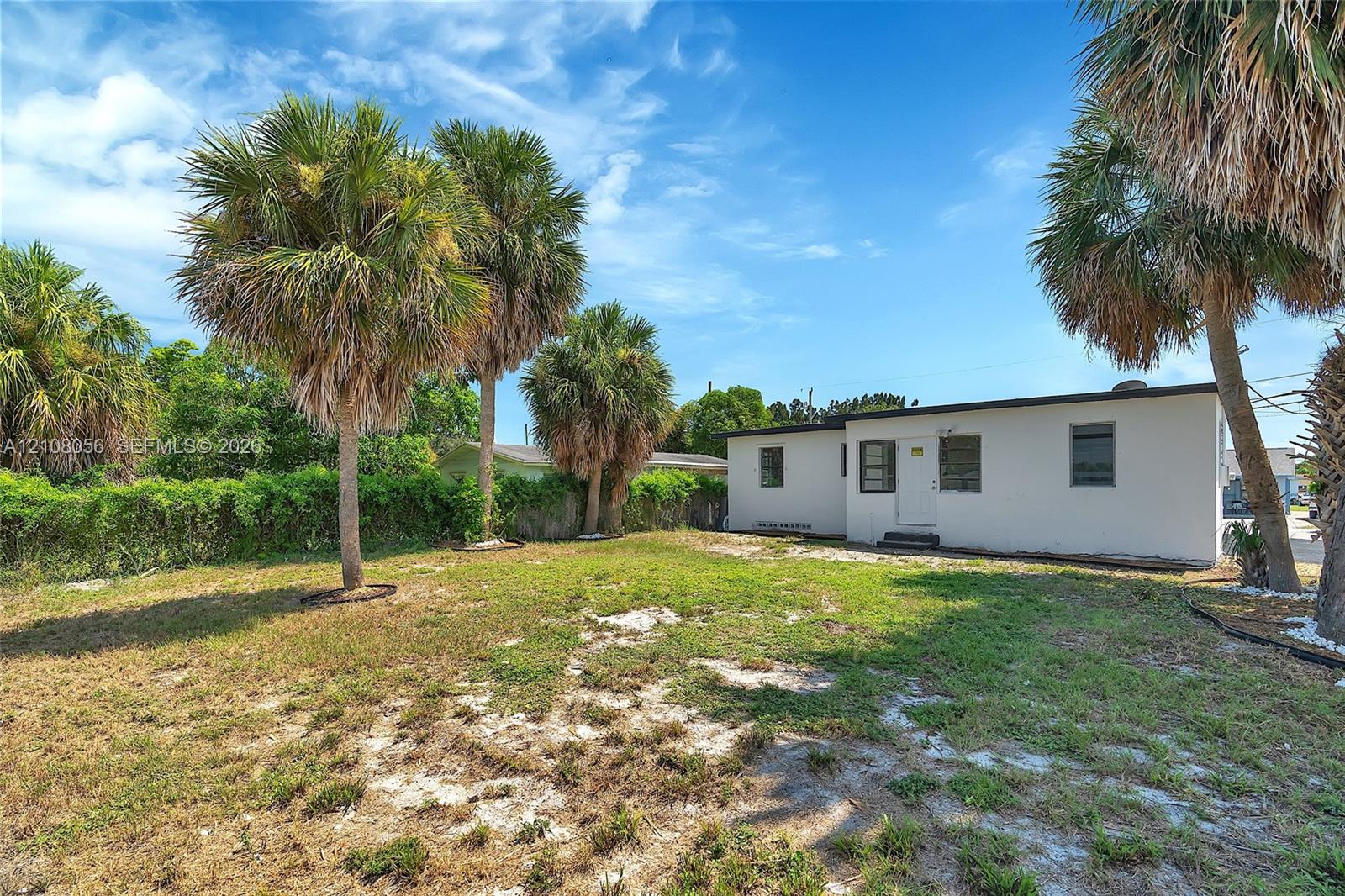 Exterior grounds featuring mature palm trees, a spacious open lawn area, and white stucco siding