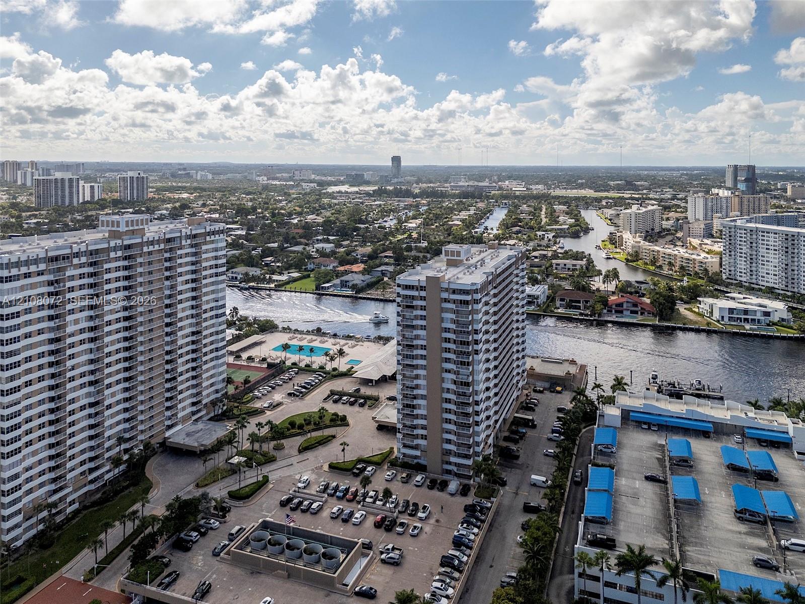 Aerial perspective of high-rise structures featuring paved surface parking, covered parking tiers, and waterfront proximity