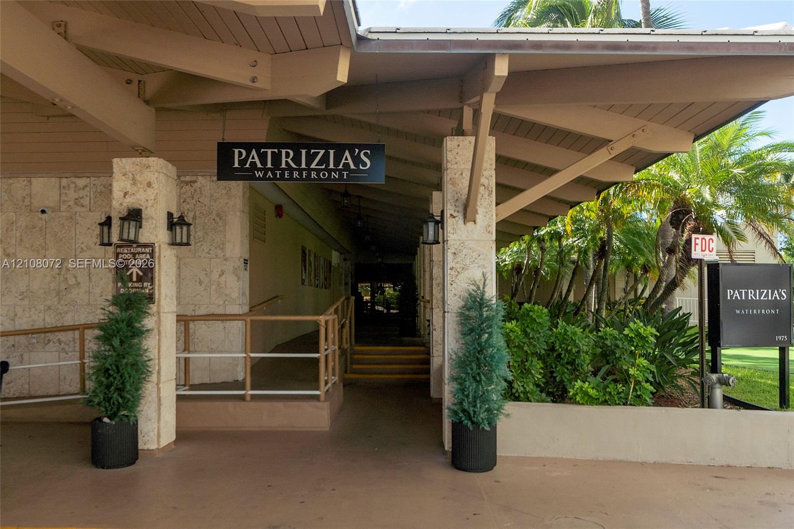Covered entryway featuring natural stone column cladding, exposed beam ceiling structure, and metal handrails