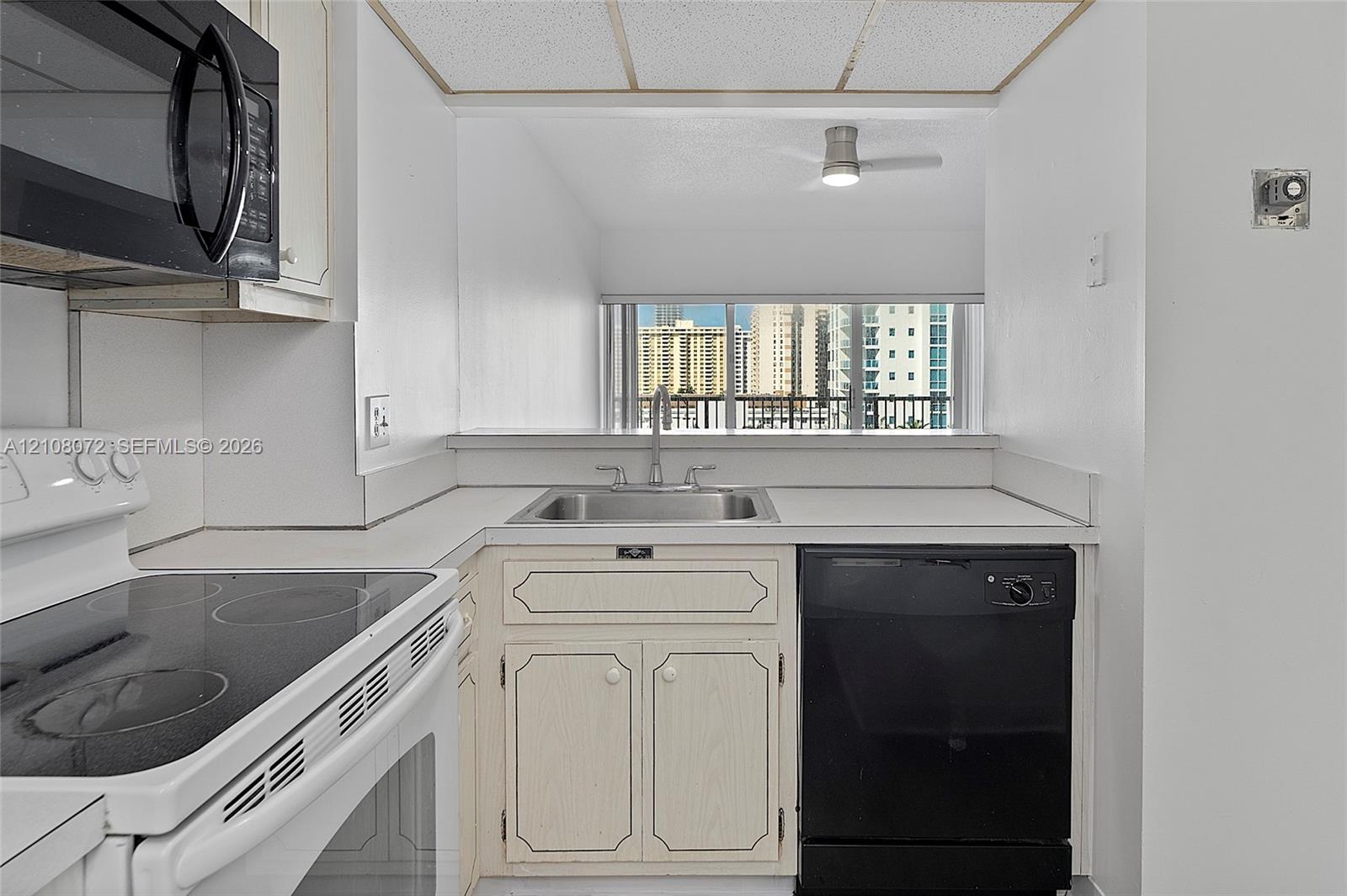 Kitchen featuring white cabinetry, integrated stainless steel sink with metal faucet, black dishwasher, and black over-the-range microwave