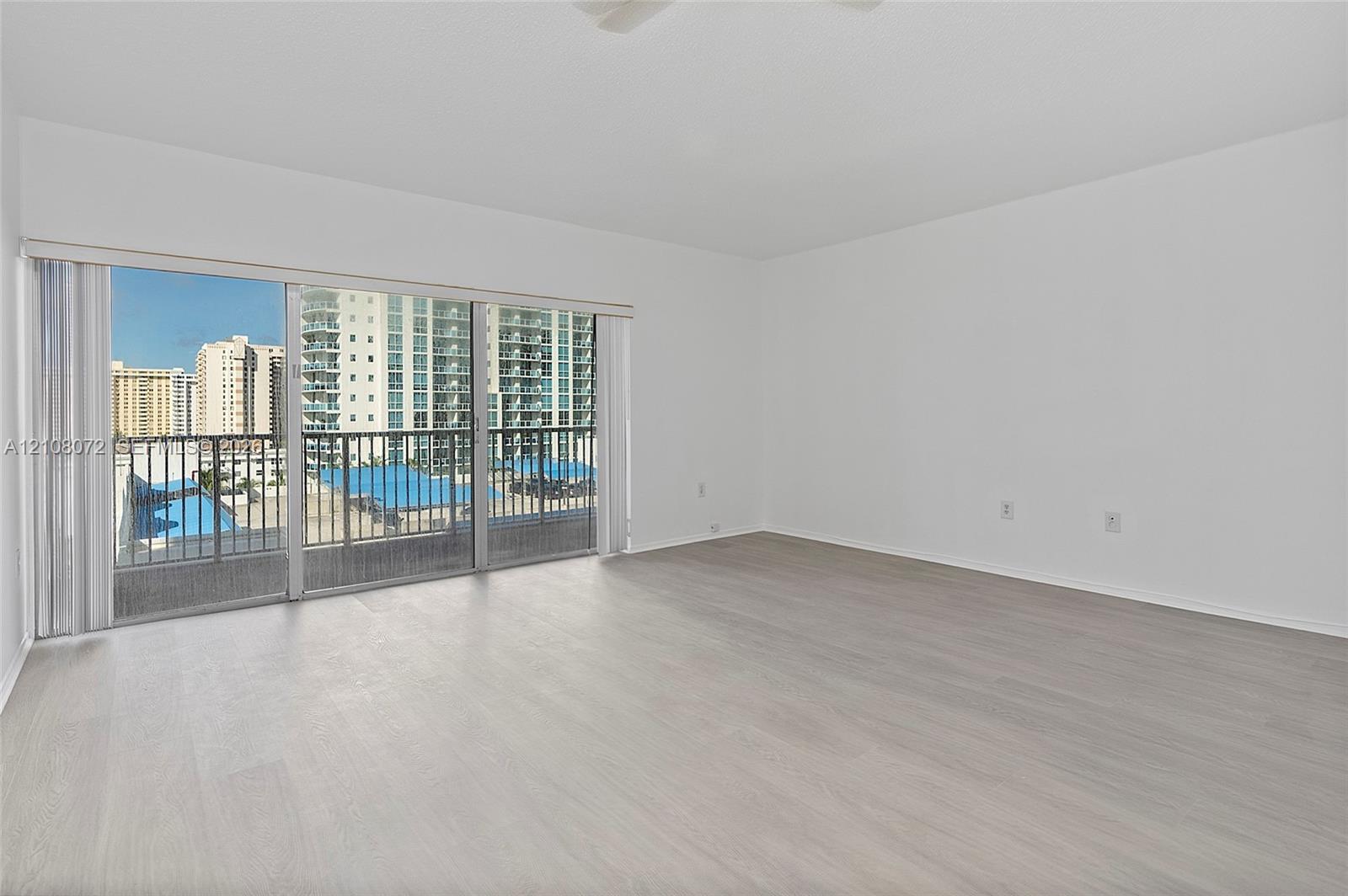 Open-concept interior featuring light wood-finish flooring, sliding glass balcony doors, and a metal-railed balcony