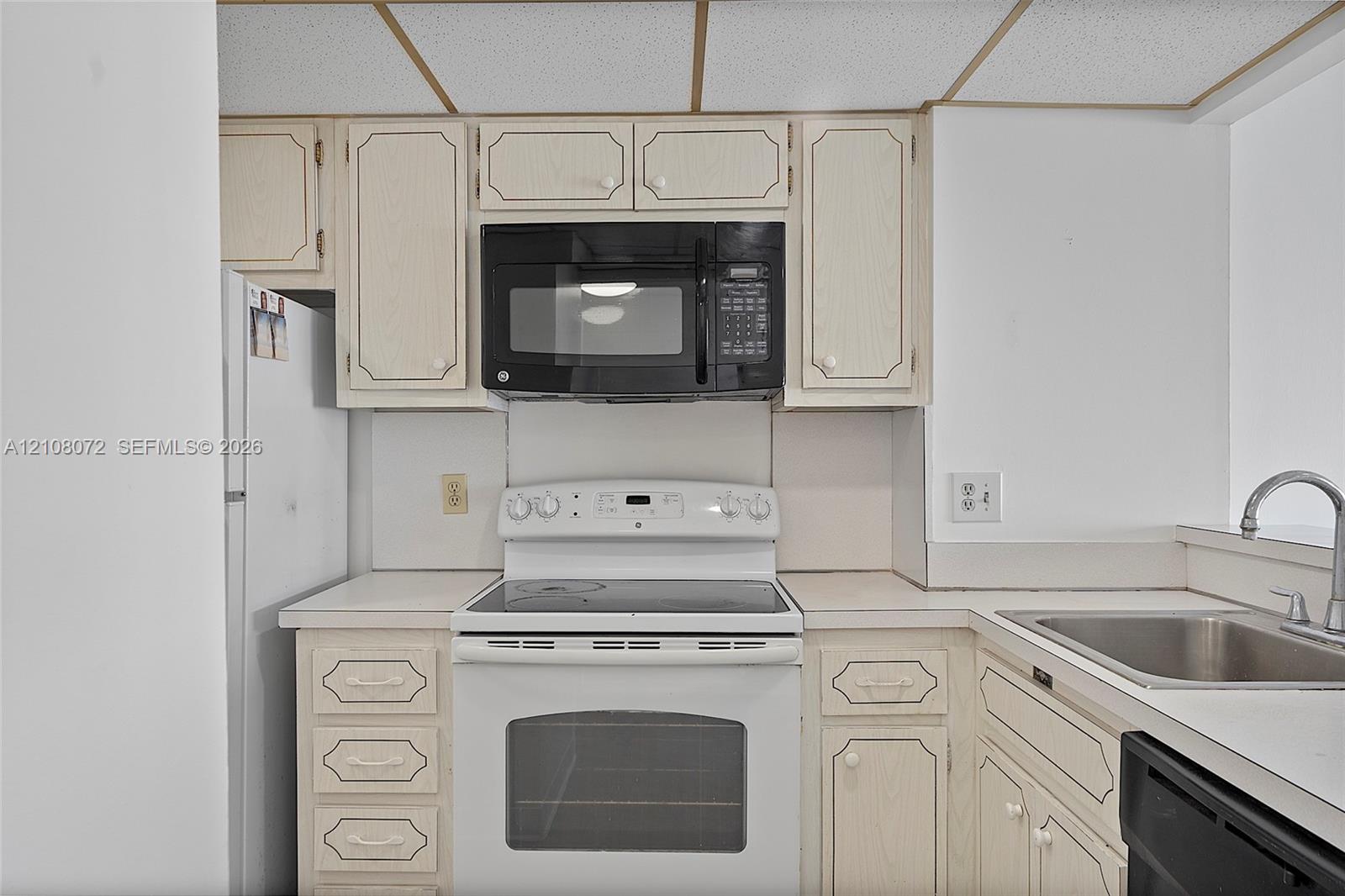 Kitchen featuring neutral-toned cabinetry, a built-in black microwave, a white electric range, a stainless steel sink with a chrome faucet, and integrated appliance placement