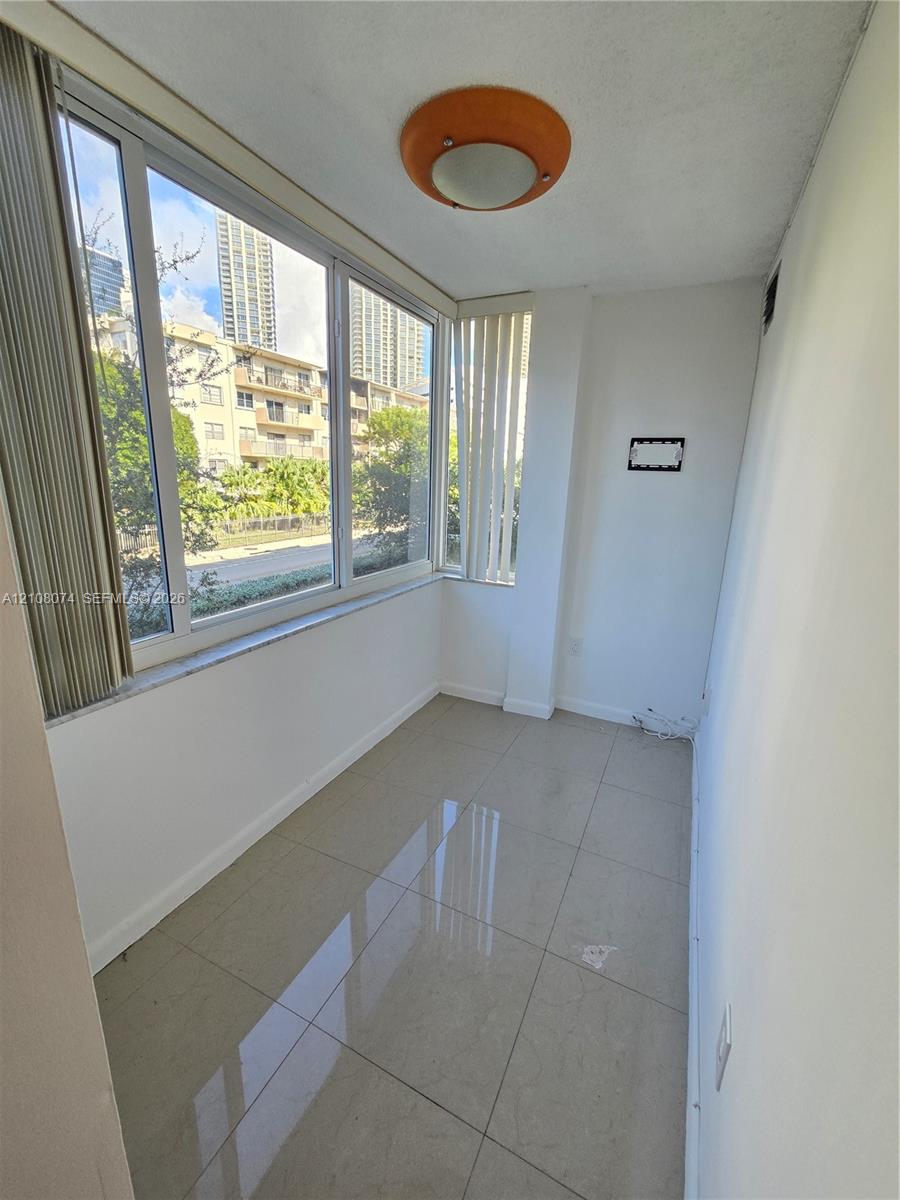 Enclosed space featuring oversized windows, light-tone tile flooring, and a flush-mount dome light fixture Enclosed space featuring oversized windows, light-tone tile flooring, and a flush-mount dome light fixture