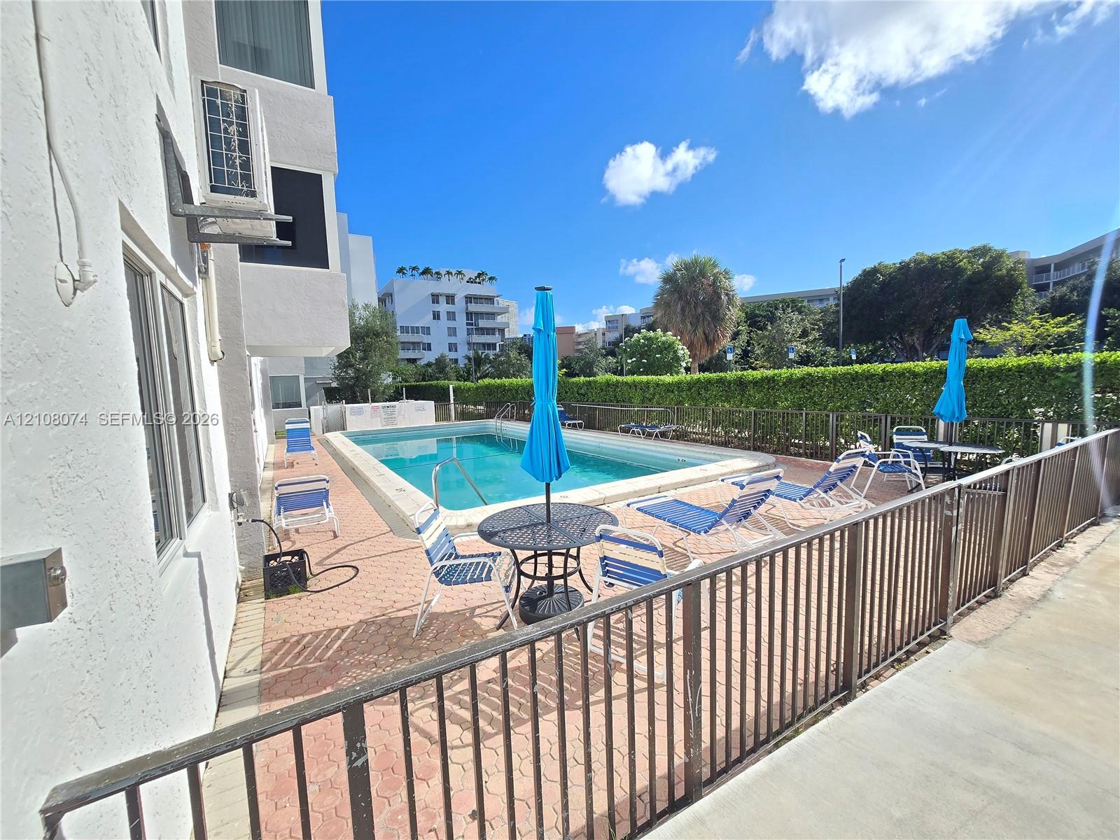 Outdoor swimming pool area featuring a paved deck, metal perimeter fencing, and established perimeter hedging