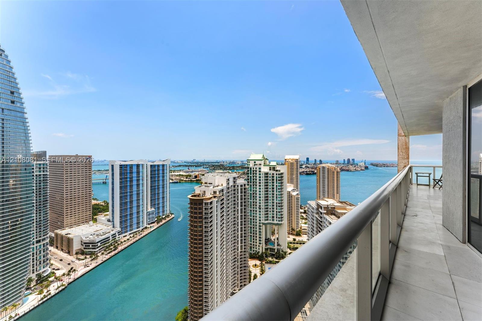 Covered balcony featuring neutral tile flooring, glass and metal railings, and panoramic coastal and metropolitan skyline scenery