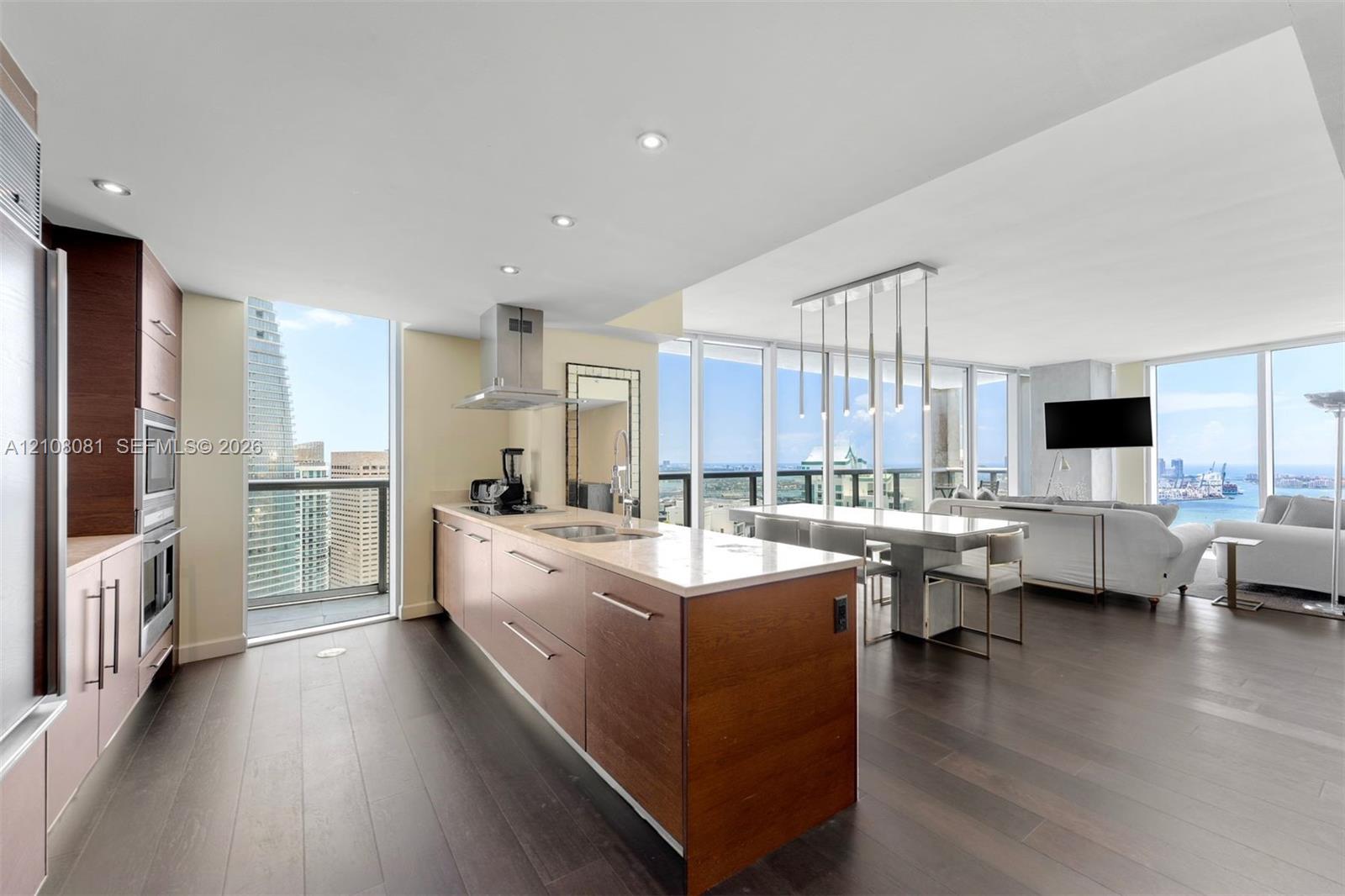 Kitchen featuring flat-panel wood cabinetry, stone countertops, stainless steel appliances, wood-finish flooring, and floor-to-ceiling windows