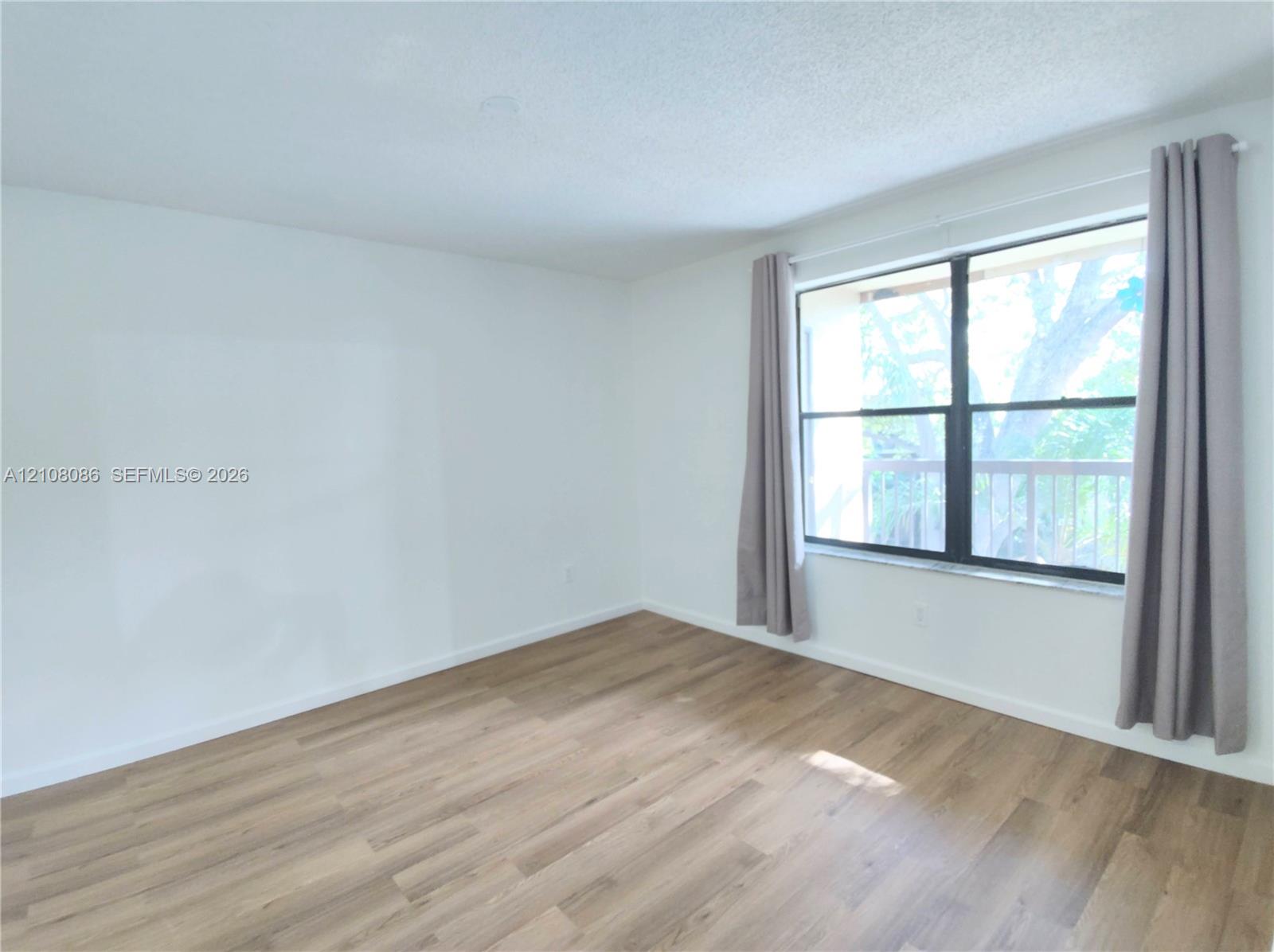 Room featuring wood-finish flooring, white walls, and a large window with a stone sill