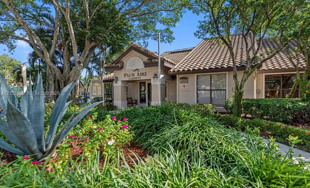 Exterior featuring a tiled roof, stucco facade, and lush professional landscaping with mature trees and native greenery