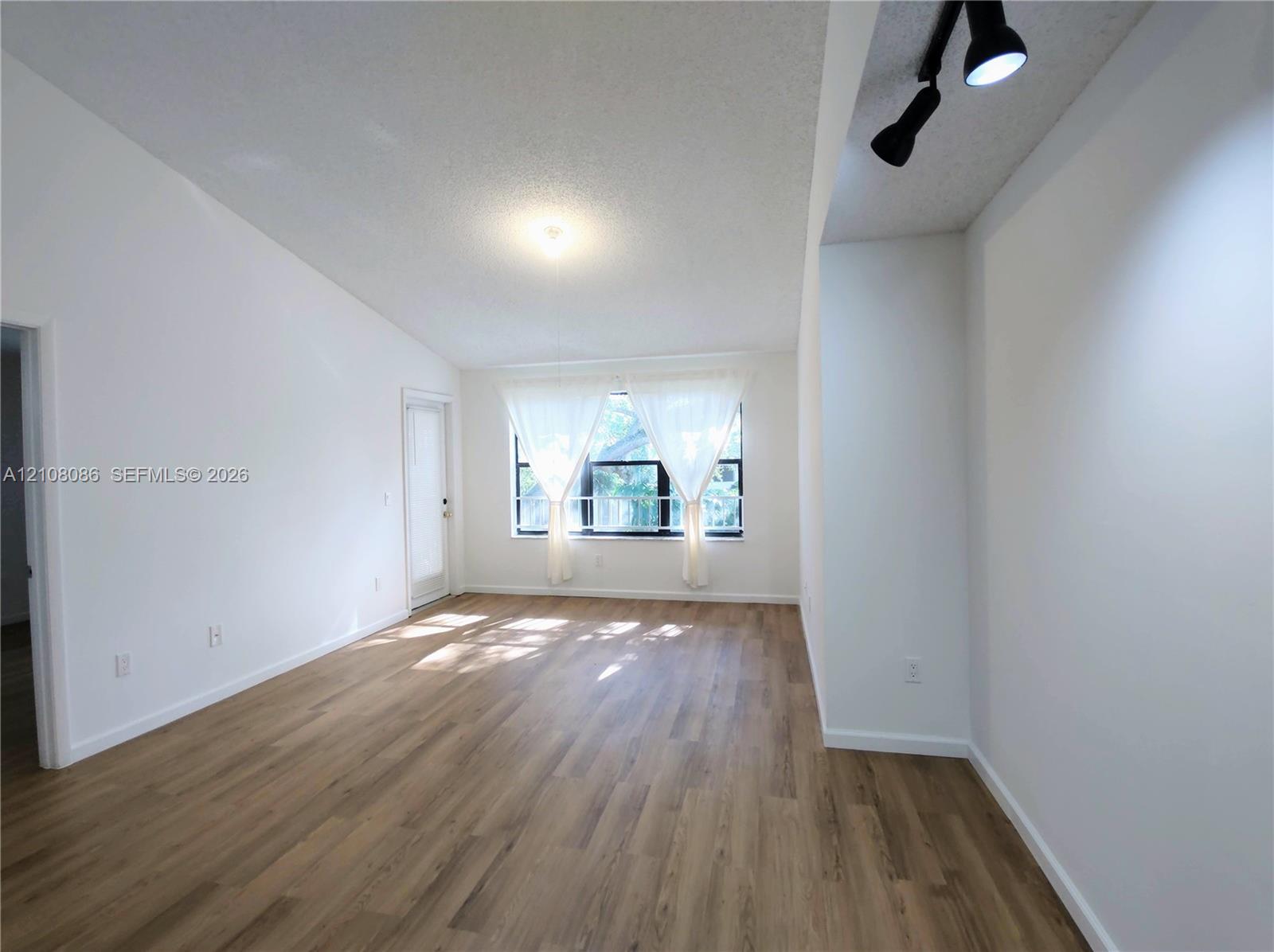 Vaulted ceiling featuring neutral wall finishes, wood-finish flooring, multi-pane window, and adjustable track lighting