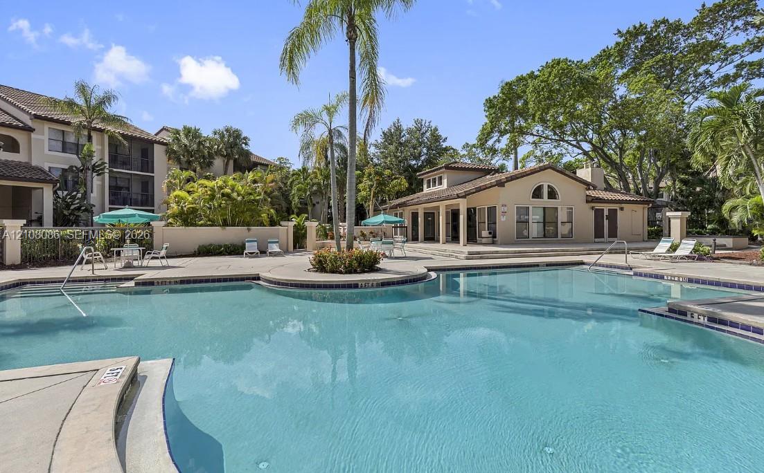Community swimming pool featuring a concrete deck, tiled edge, perimeter wall, and surrounding palm trees