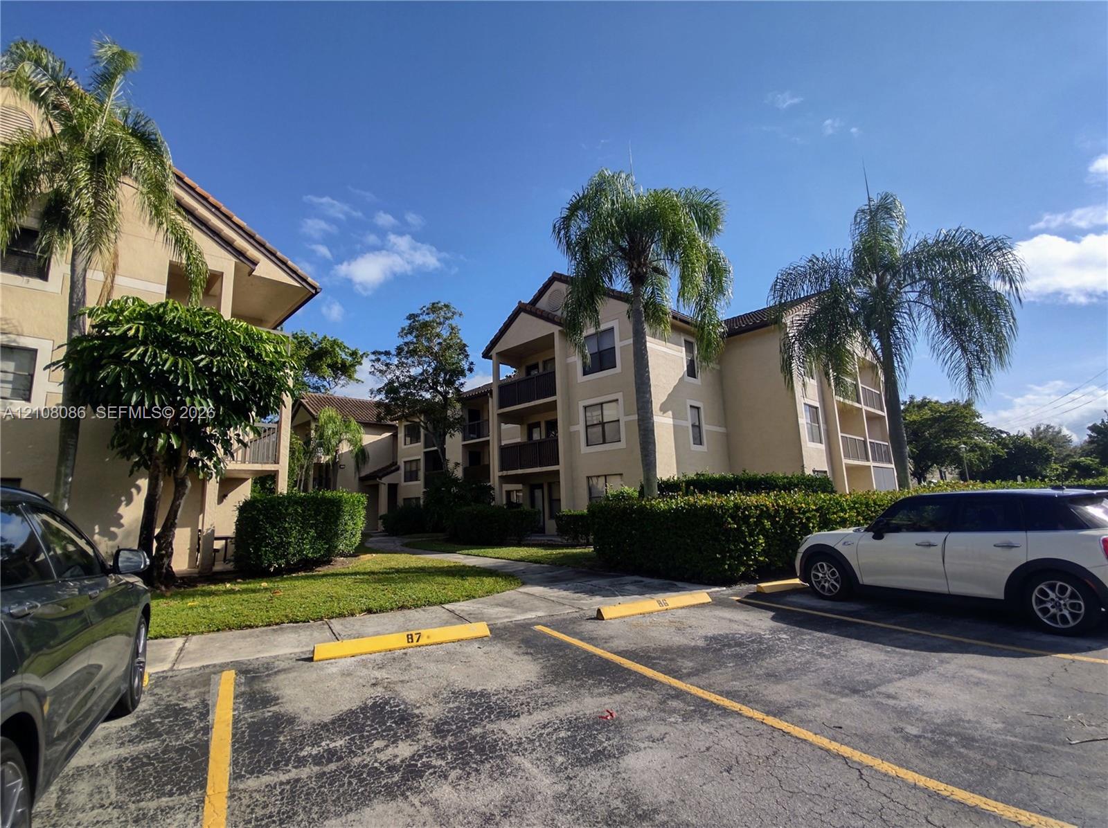 Multi-story residential building exterior featuring stucco siding, gabled rooflines, recessed balconies, and mature palm trees