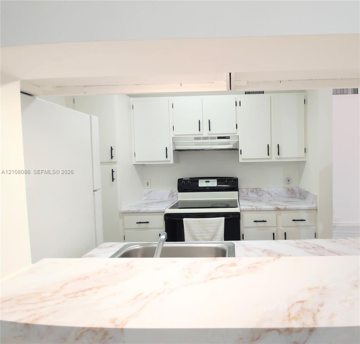 Kitchen featuring white cabinetry with dark hardware, stone-patterned countertops, a stainless steel sink, and a built-in range hood