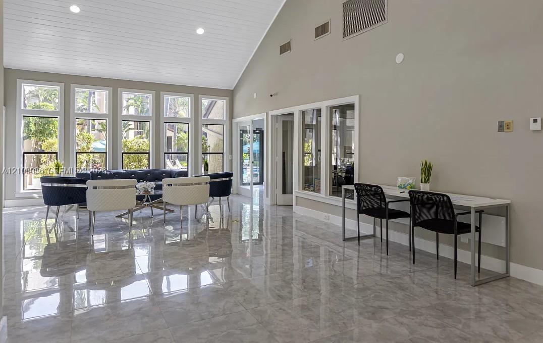 Vaulted ceiling with tongue-and-groove paneling, polished stone-finish tile flooring, and floor-to-ceiling windows