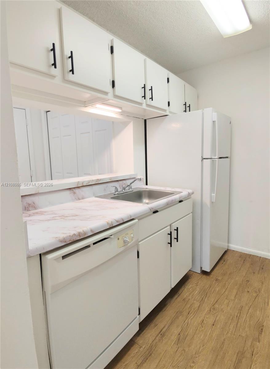 Kitchen featuring white cabinetry with matte black hardware, stone-pattern laminate countertops, stainless steel sink with a dual-handle faucet, and wood-finish flooring