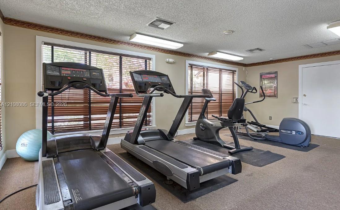 Fitness center featuring wall-to-wall carpeting, multiple windows with horizontal blinds, and overhead fluorescent lighting