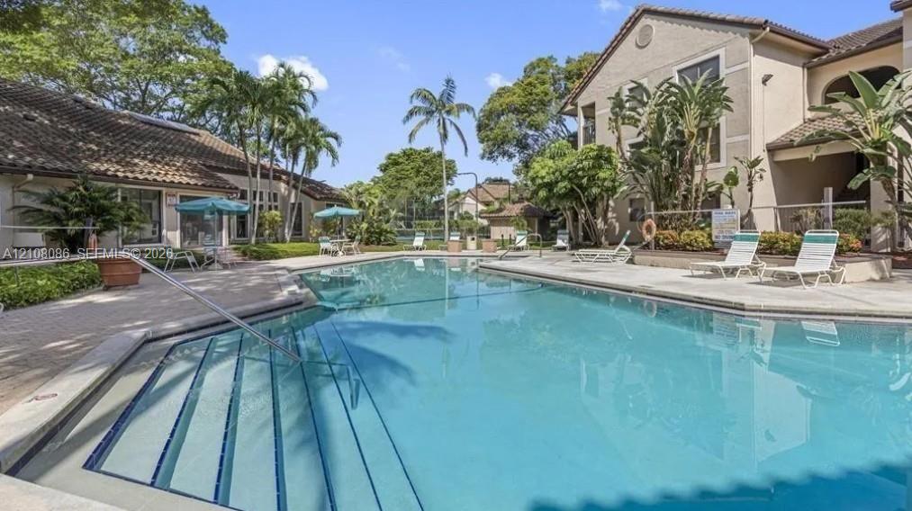 Community swimming pool featuring a concrete deck, built-in entry steps with handrails, and surrounding tropical landscaping