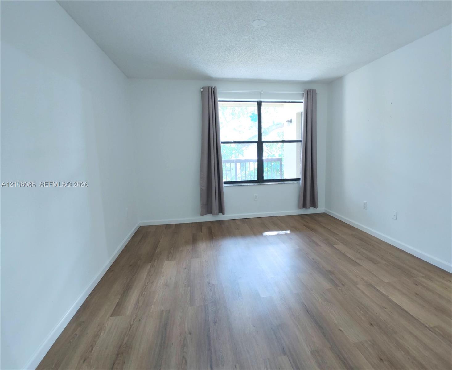Neutral interior space featuring wood-finish flooring, white walls, and a window with black framing