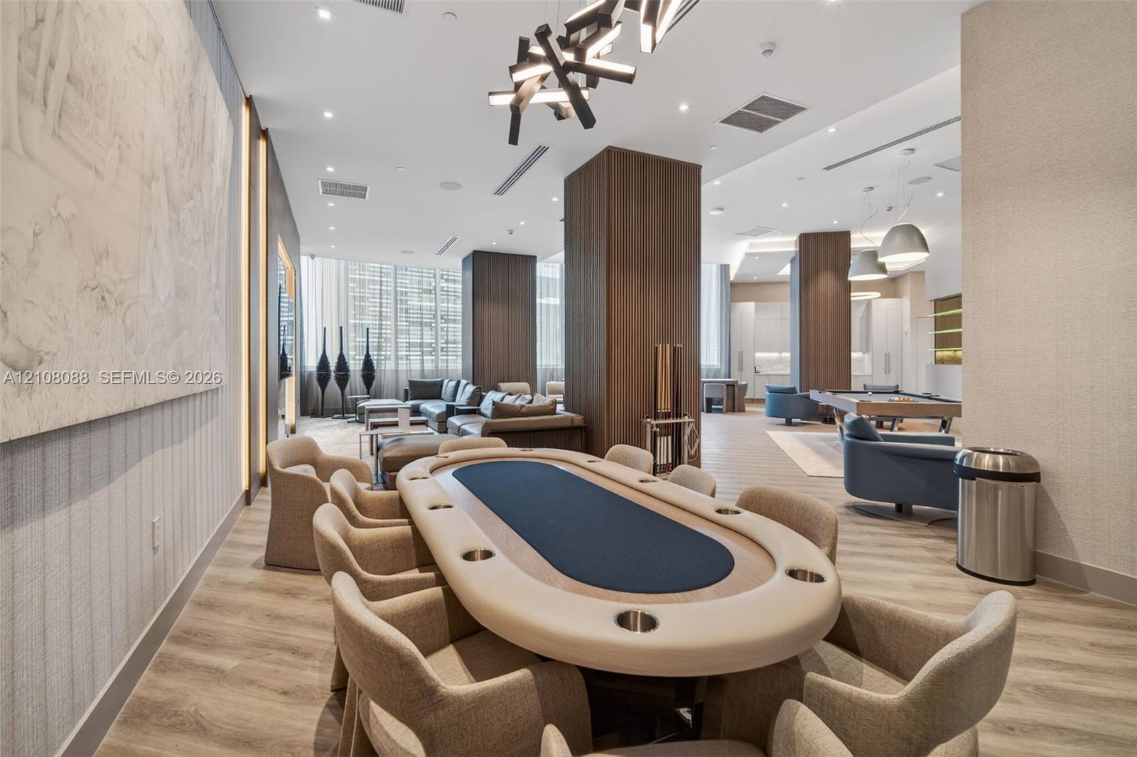 Expansive common area featuring wood-finish flooring, floor-to-ceiling windows, modern geometric pendant lighting, built-in structural columns with wood veneer, and recessed ceiling lighting