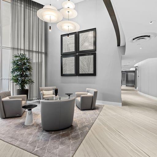 Double-height floor-to-ceiling windows, modern multi-tiered pendant lighting, and polished stone-finish flooring