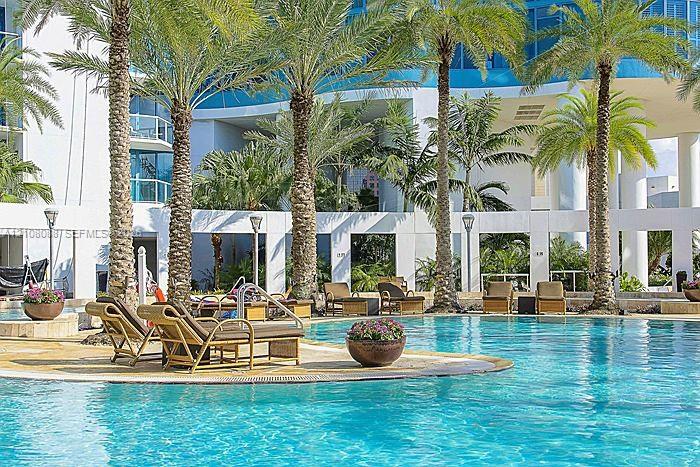 Swimming pool with tiled decking, surrounded by mature palm trees and architectural concrete columns