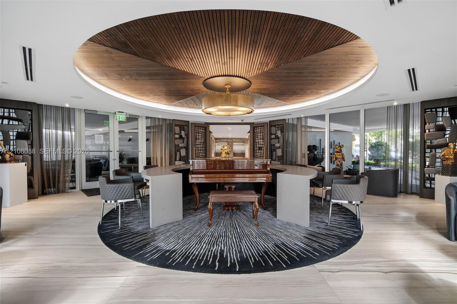 Circular recessed ceiling feature with wood-slat detailing, central custom drum chandelier, light-toned wood-finish flooring, and curved semi-circular stone-surface built-in desk