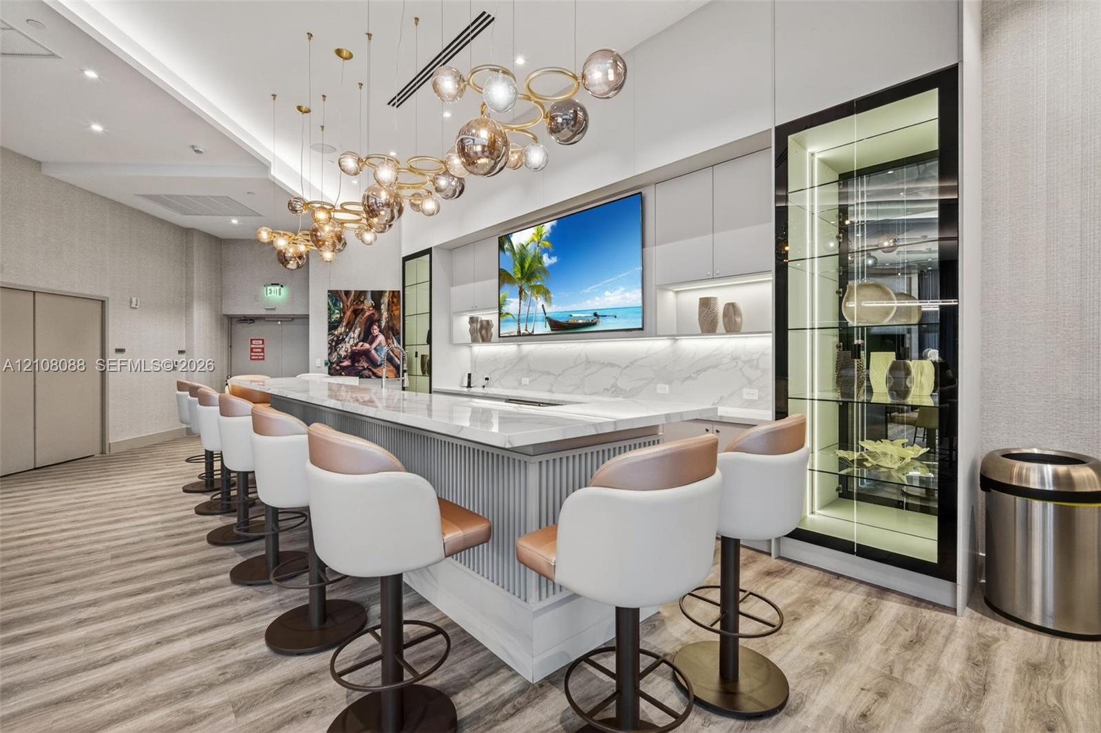 Custom bar area featuring a stone-topped counter with vertical millwork paneling, stone backsplash, sculptural multi-sphere chandelier, and a floor-to-ceiling built-in illuminated display cabinet