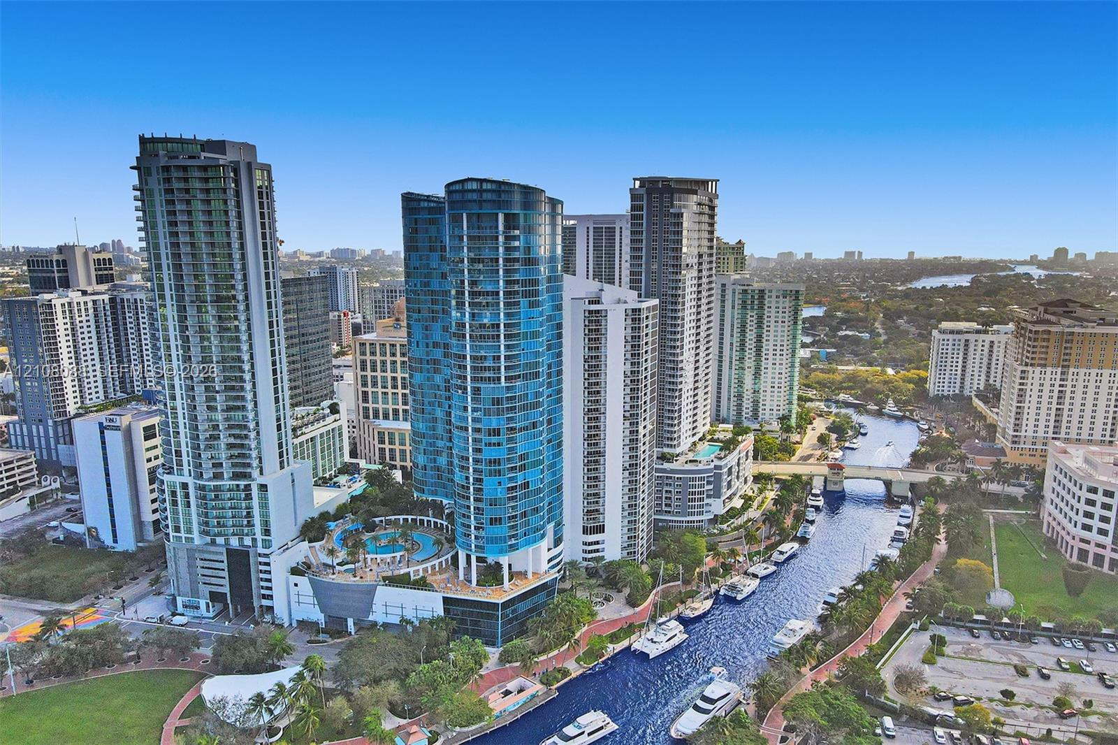 Aerial perspective of high-rise urban towers featuring glass-facade architecture, a multi-level swimming pool terrace, and water-front placement along a canal