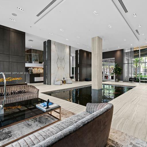 Lobby area featuring large-format tile flooring, a centered indoor water feature, stone-accented columns, floor-to-ceiling glass windows, and recessed ceiling lighting