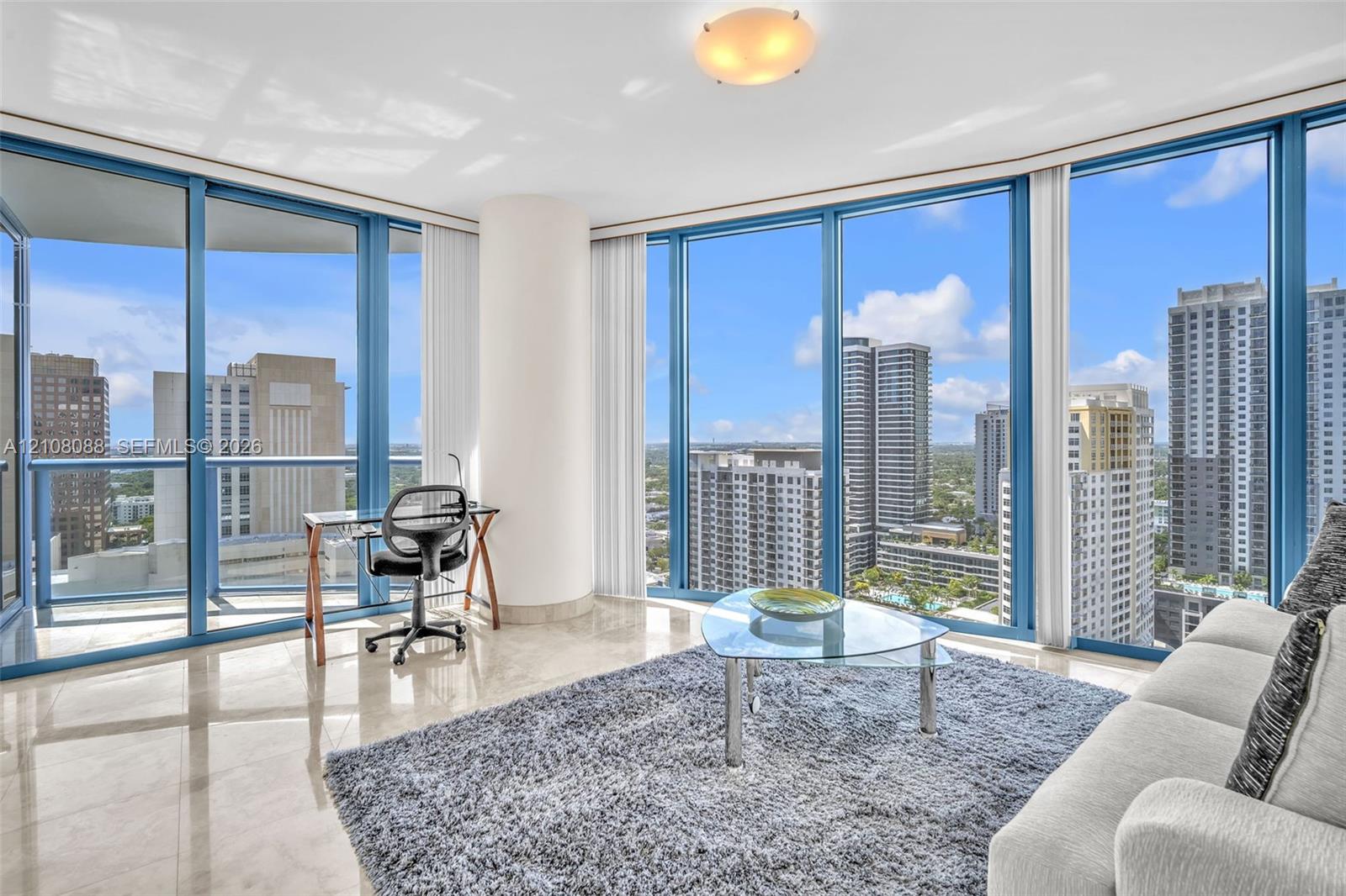 Floor-to-ceiling windows featuring panoramic urban scenery, polished stone flooring, and a glass balcony railing