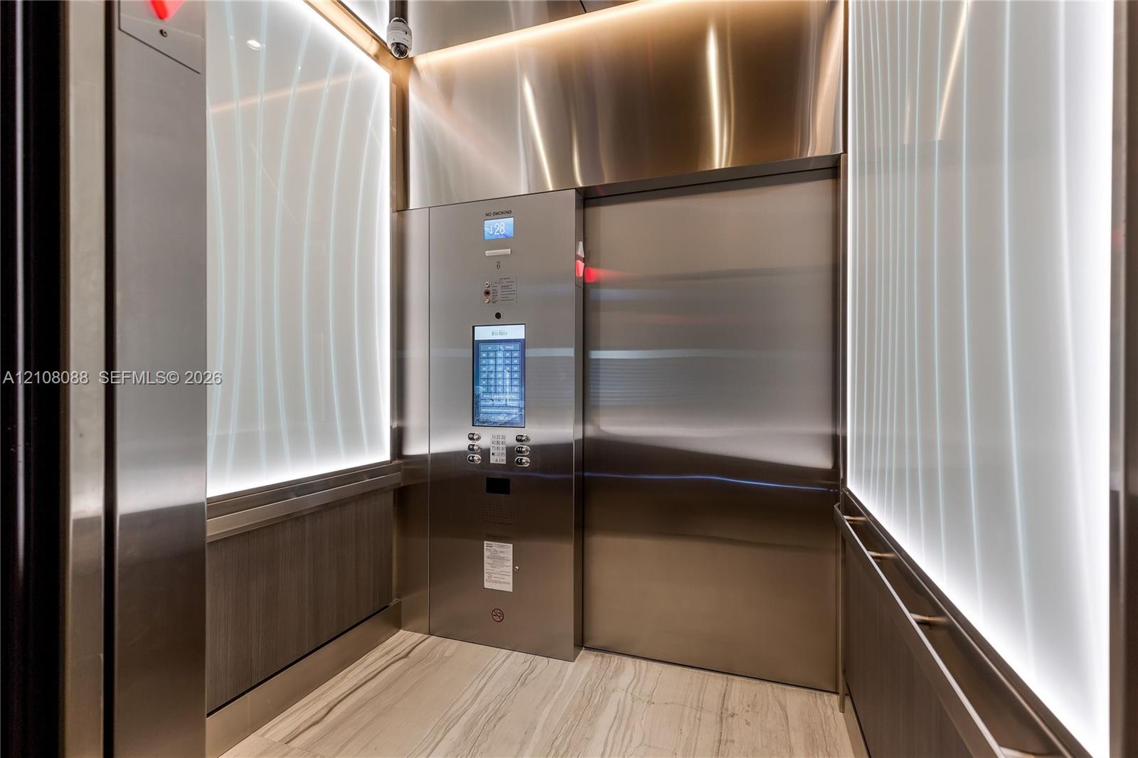 Elevator interior featuring brushed stainless steel paneling, illuminated frosted glass wall accents, stone flooring, and an integrated digital touchscreen control interface