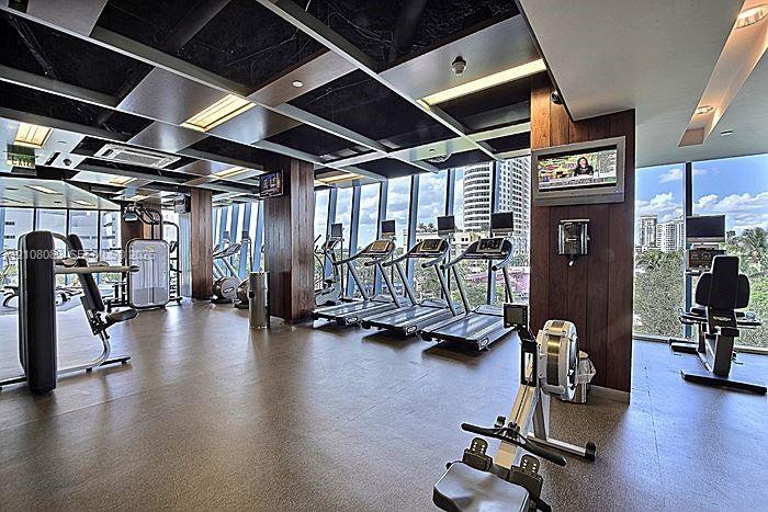 Fitness facility featuring floor-to-ceiling windows, wood-paneled structural columns, grid-patterned recessed ceiling panels, and neutral resilient flooring