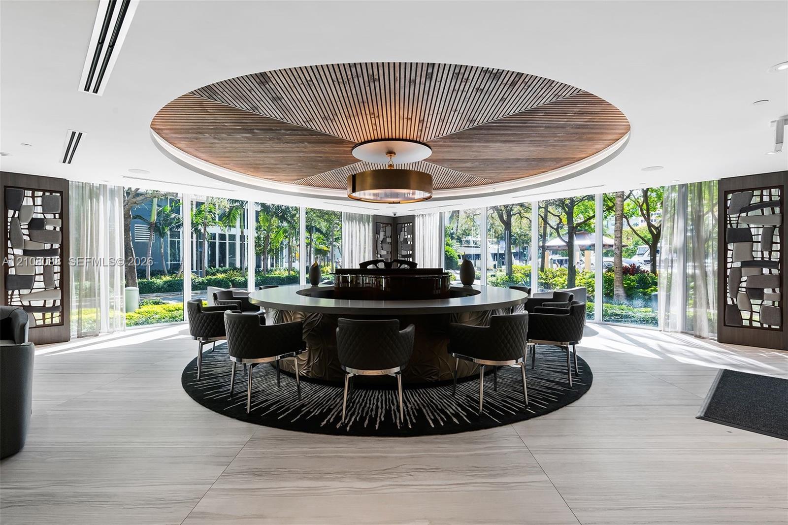 Circular architectural feature with a geometric wood-paneled ceiling inlay and central cylindrical light fixture, surrounded by floor-to-ceiling windows and large-format tile flooring