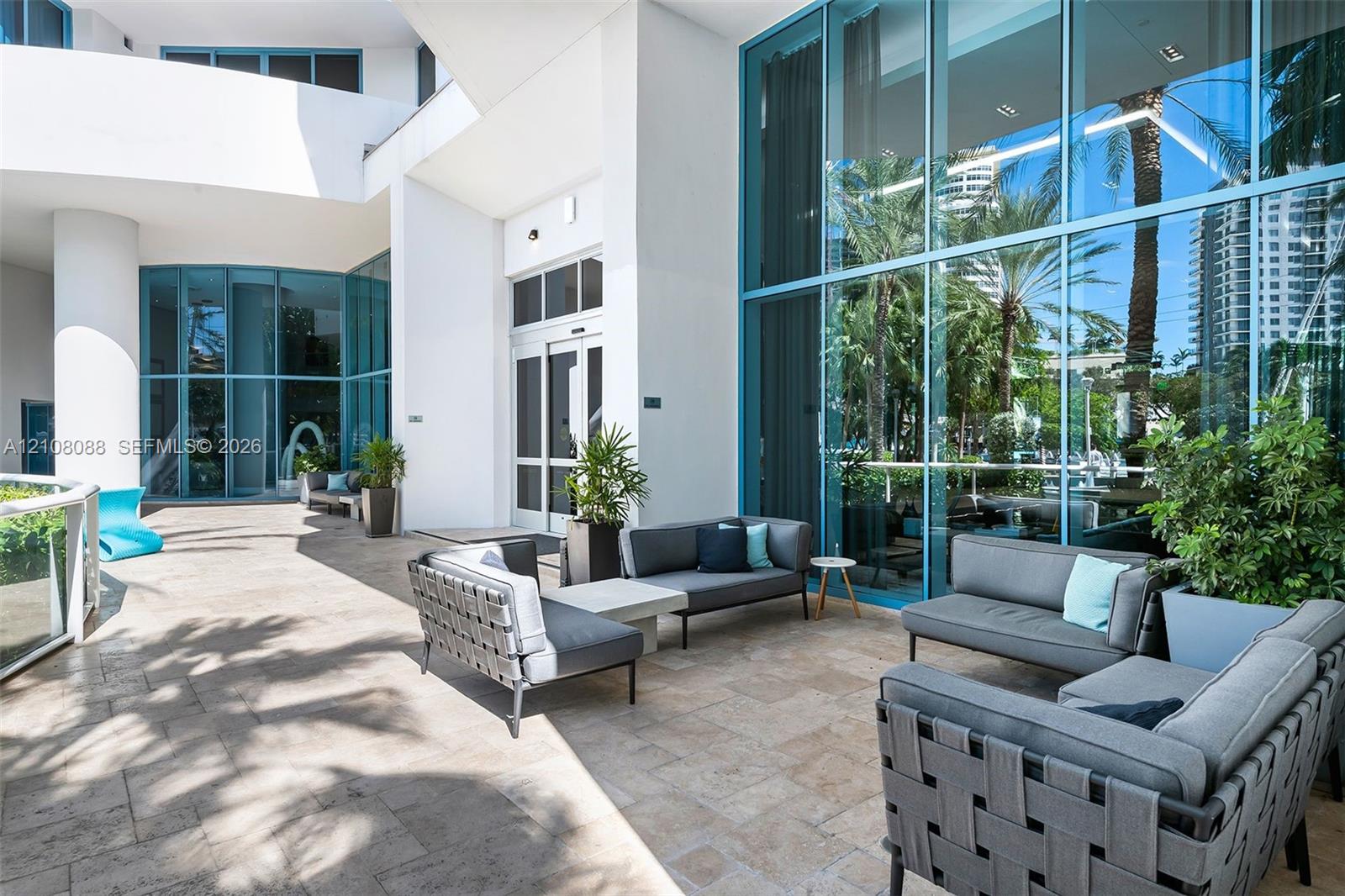 Covered terrace featuring stone tile flooring, floor-to-ceiling glass paneling, and prominent white architectural columns